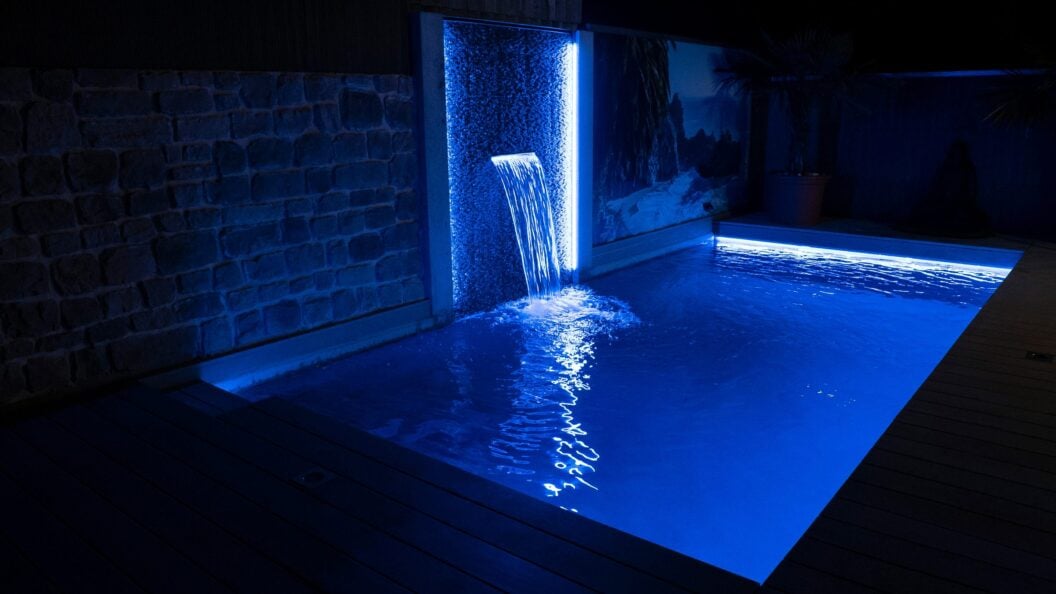Beleuchtete Wasserwand an einem Pool bei Nacht