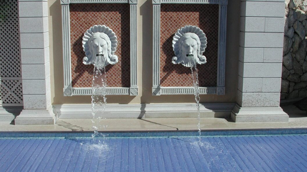 Zwei Wasserspeier mit Löwenköpfen an einer Poolwand