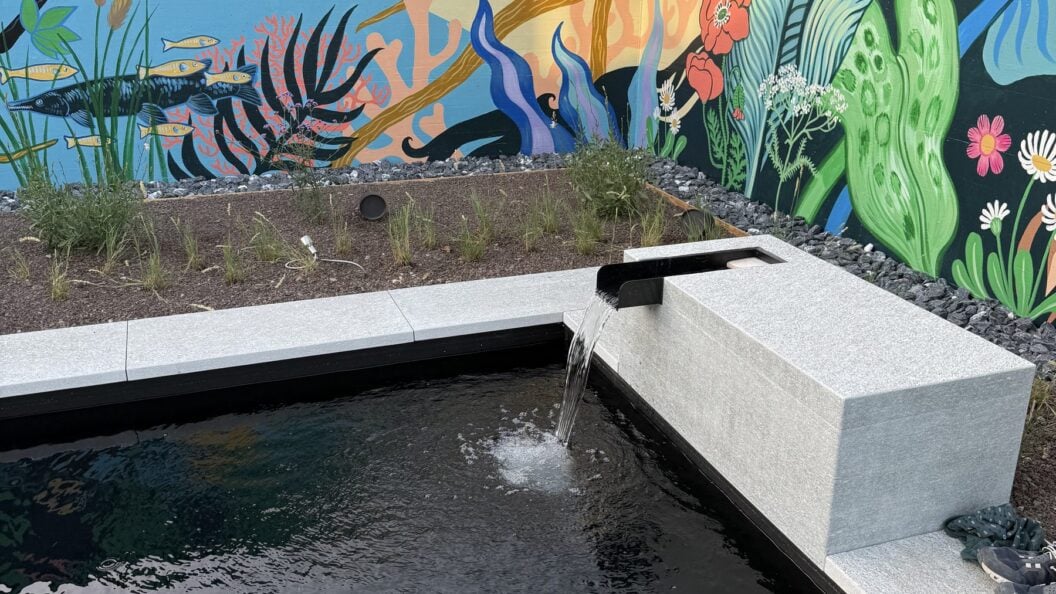 Wasserauslauf aus einem Betonblock vor einer bemalten Gartenmauer